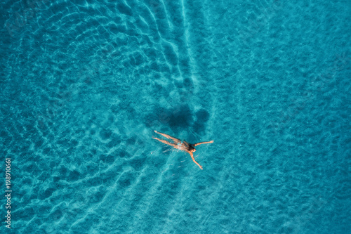 Aerial view of swimming woman in Blue Lagoon. Mediterranean sea in Oludeniz, Turkey. Summer seascape with girl, clear azure water, waves in sunny day. Transparent water. Top view from flying drone