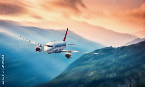 Airplane in motion. Aircraft with motion blur effect is flying over hills and mountains at sunset. Passenger airplane, blurred clouds. Passenger aircraft in motion. Business travel. Commercial.Concept