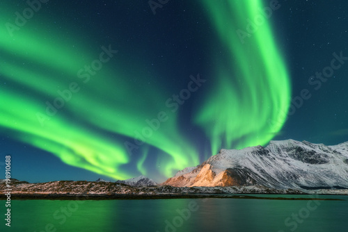 Aurora borealis. Lofoten islands, Norway. Aurora. Green northern lights. Starry sky with polar lights. Night winter landscape with aurora, sea with sky reflection and snowy mountains. Nature. Travel