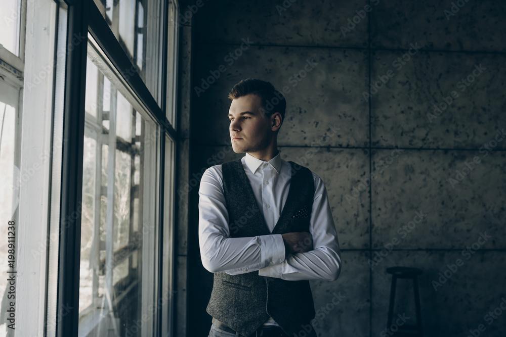 Young beautiful man staying near the window on a gray background. Young beautiful man staying near the window on a gray background.