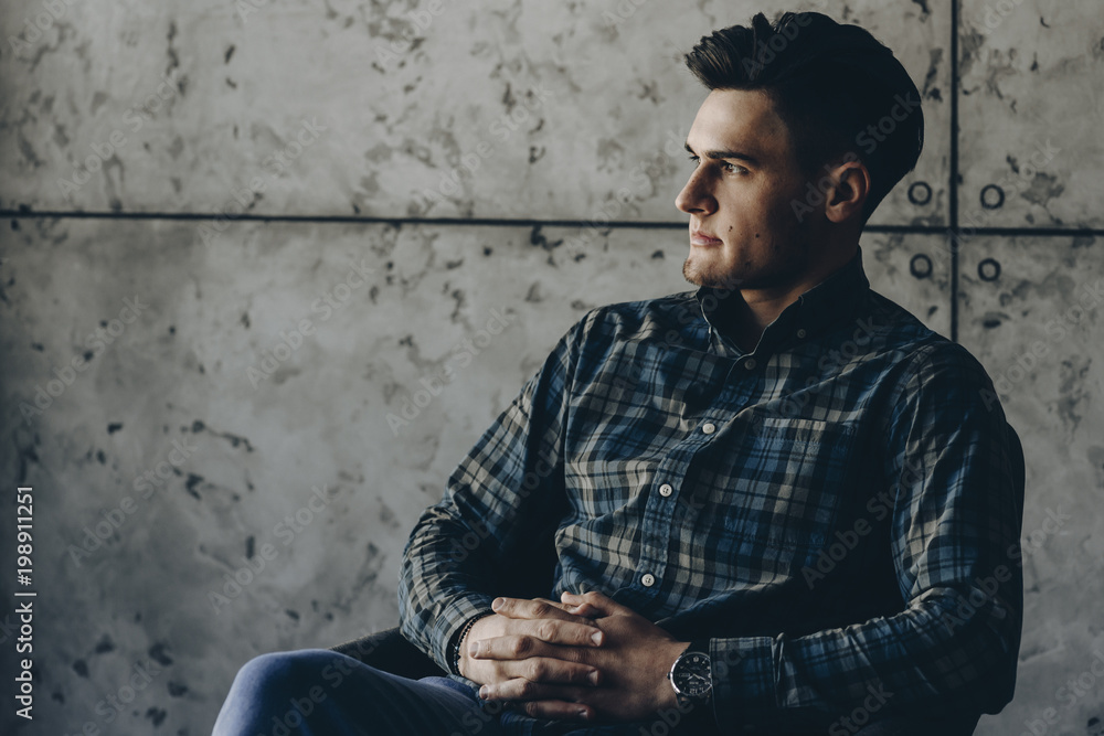 Adult handsome man sitting on a chair looking away on a gray background. Adult handsome man sitting on a chair looking away on a gray background.