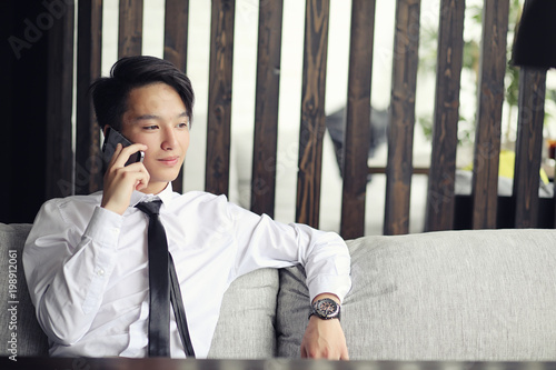 A young Asian businessman is waiting for a partner in a cafe. Bu