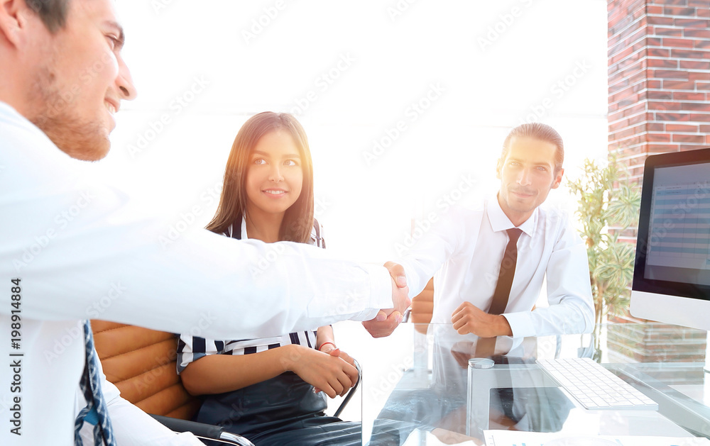 Obraz premium men shaking hands and smiling while sitting at the desk