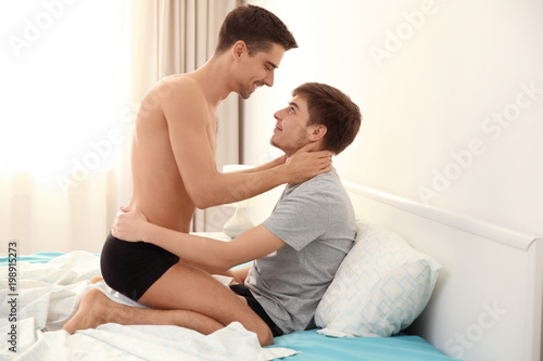 Foto Young gay couple together on bed in light room