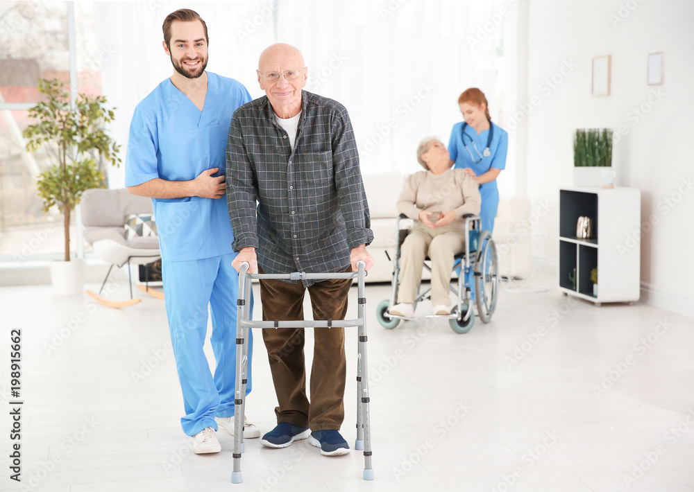 Senior man with walking frame and young caregiver at home Senior man with walking frame and young caregiver at home