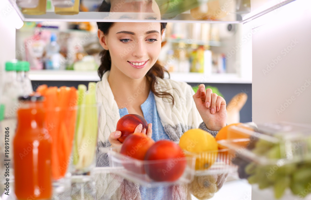 Portrait of female standing near open fridge full of healthy food, vegetables and fruits. Portrait of female Portrait of female standing near open fridge full of healthy food, vegetables and fruits. Portrait of female