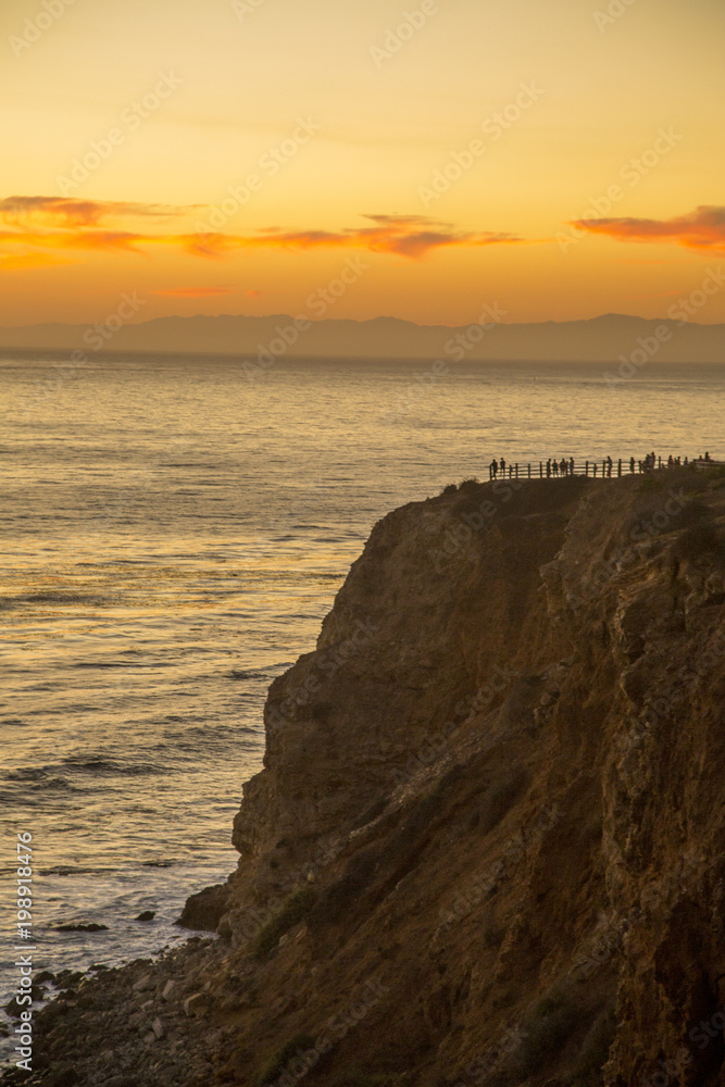Scenic cliffs with people overlooking the Pacific Ocean with sun setting