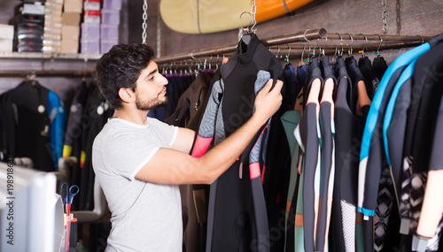 man holding and choosing suit for surfing in the shop