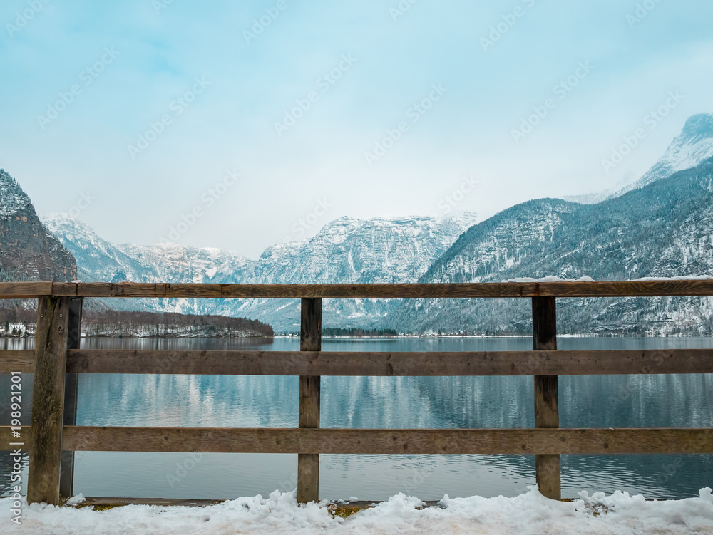 wooden fence in hallstatt lake landscape view winter season snow tree reflection blue sky mountain