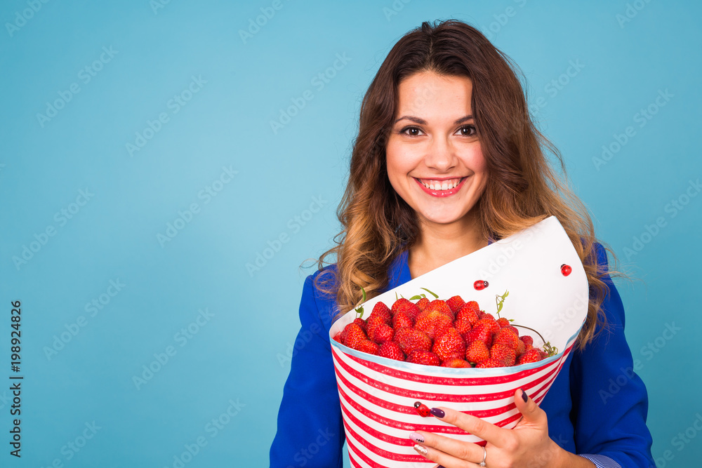 Young woman holding bouquet of strawberries on blue background. Young woman holding bouquet of strawberries on blue background.