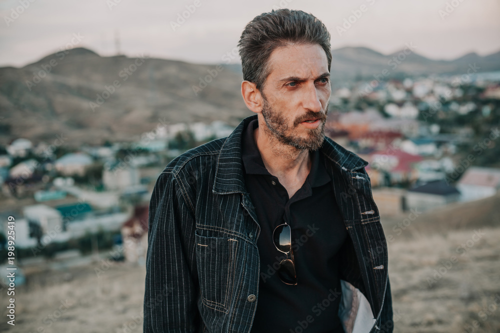 young man with beard against backdrop of mountains young man with beard against backdrop of mountains