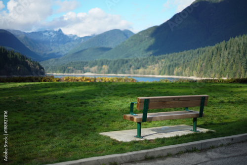 Empty park bench in front of lake and mountains