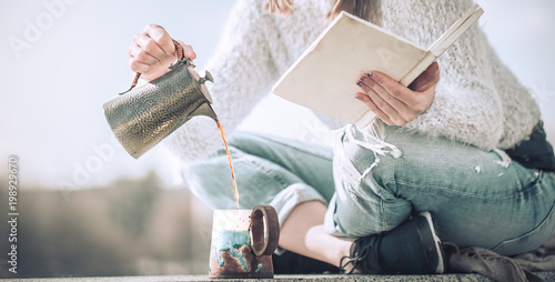 girl drinks coffee and reads book outdoors, concept of hot drinks and relaxation