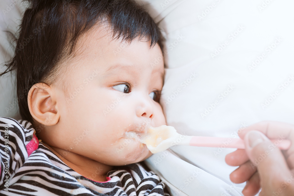 Mother feeding cute asian baby girl with a spoon at home. Little baby girl eating her meal with innocence. Mother feeding cute asian baby girl with a spoon at home. Little baby girl eating her meal with innocence.
