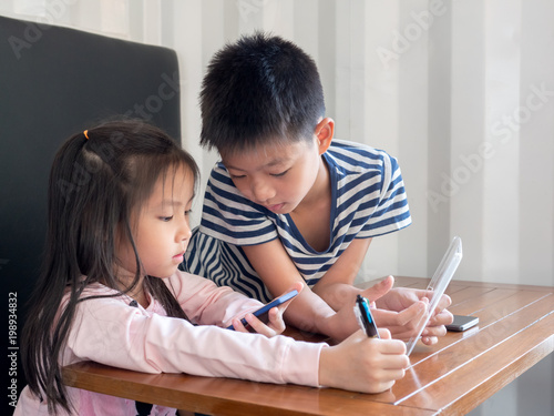 Asia pretty little girl and handsome boy play mobile phone, looking to something in their phone