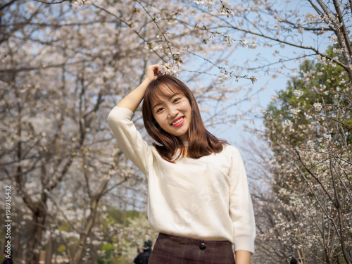 Outdoor portrait of beautiful young Chinese girl smiling among blossom cherry tree brunch in spring garden, beauty, summer, emotion, expression and people concept. © atiger