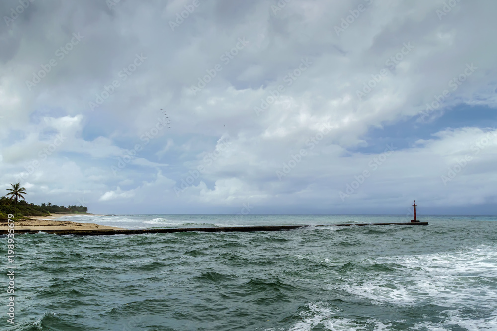 ocean coast, waves, sky, clouds, flock of pelicans flying in height, old lighthouse, breakwater