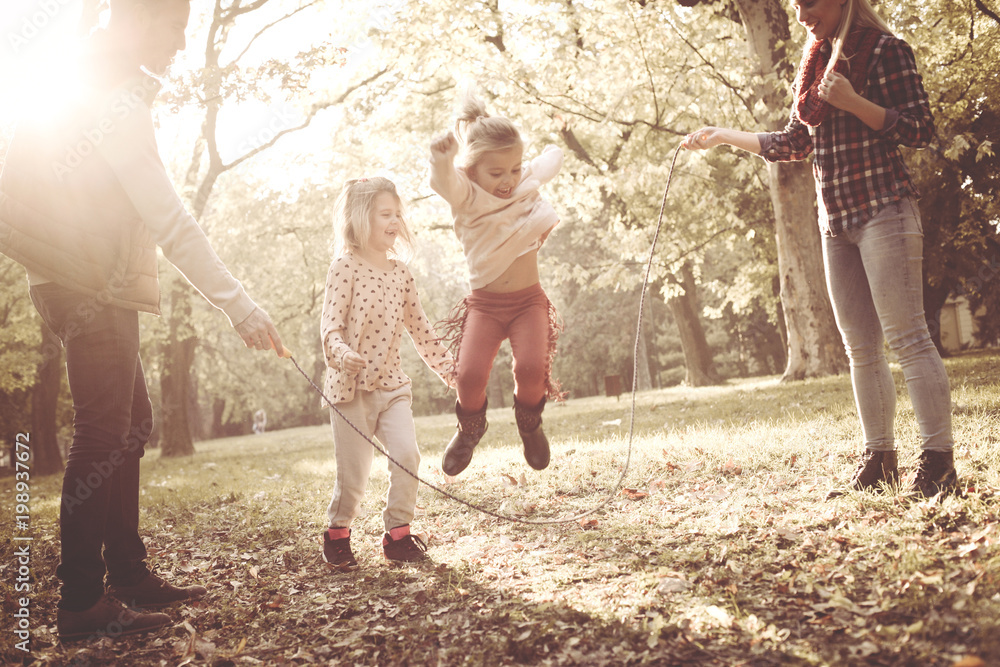 Little girls jumping across jump rope and parents holding rope in park. Little girls jumping across jump rope and parents holding rope in park.