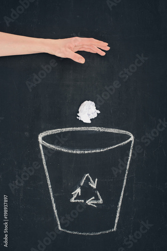 cropped shot of woman throwing crumpled paper into drawn trash bin with recycle sign on chalkboard
