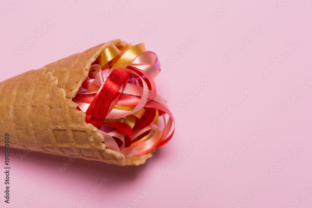 ice cream cone and colored ribbons on a pink background, copy space ice cream cone and colored ribbons on a pink background, copy space