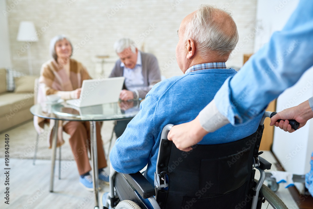 Portrait of nice senior couple smiling at friend in wheelchair coming to meet in retirement home, copy space