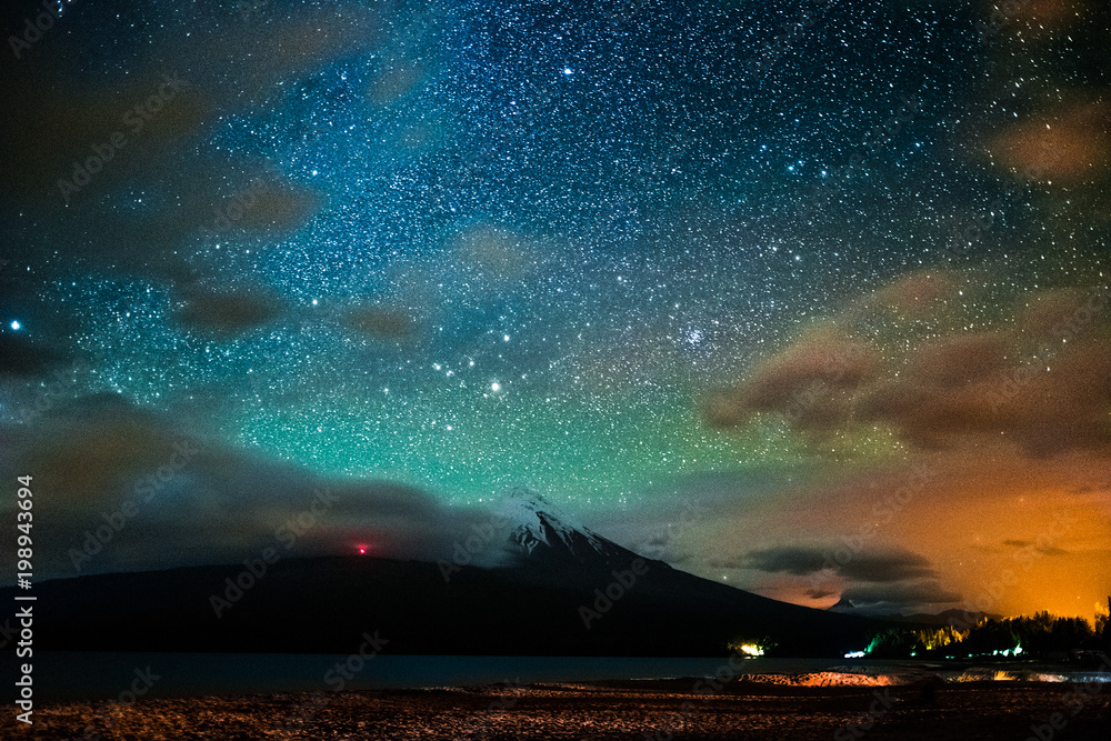 Starry sky and the volcano of Osorno with clouds highlighted by town, Chile. High level of noise