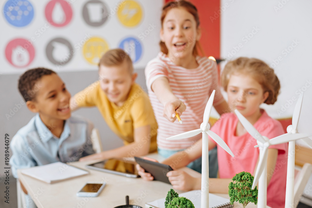 Alternative energy source. The focus being on the wind turbines standing on the table and being pointed at by a cheerful girl during the discussion about alternative energy Alternative energy source. The focus being on the wind turbines standing on the table and being pointed at by a cheerful girl during the discussion about alternative energy