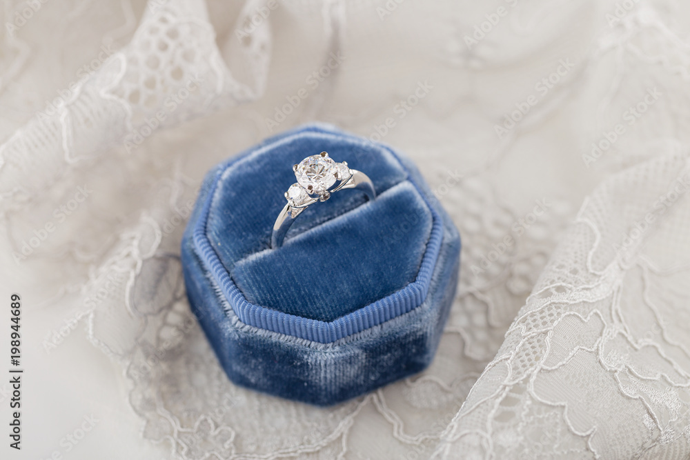 White golden wedding ring with diamonds in blue vintage velvet ring box on gray lace background White golden wedding ring with diamonds in blue vintage velvet ring box on gray lace background