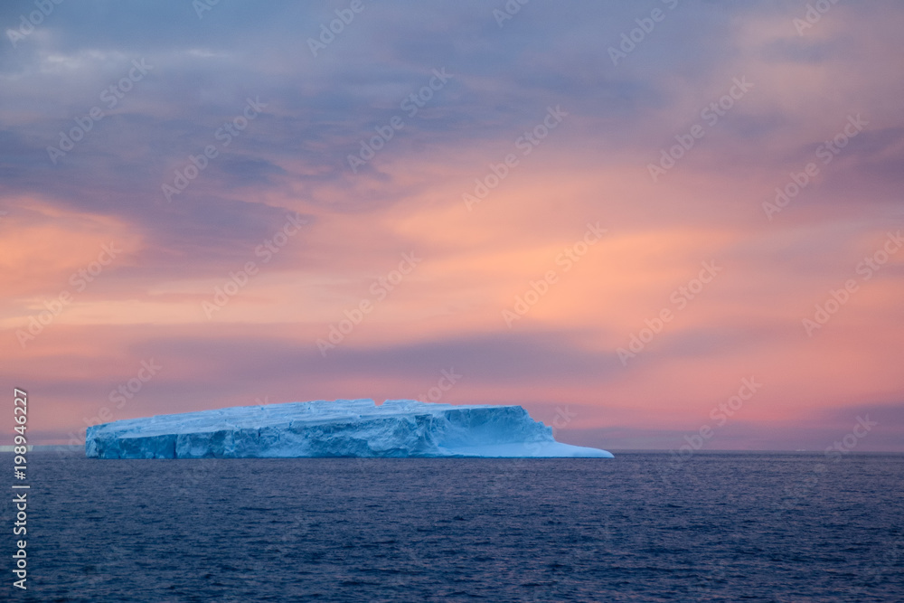 Southern Ocean Antarctica, pink and grey clouds at sunset with iceberg in foreground