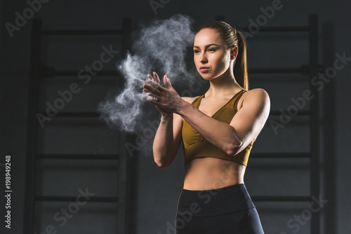 Young sportswoman spreading chalk powder in hands for exercising in sports hall