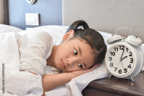 School kid suffering insomnia (sleeping disorder), mental health illness concept with Asian girl child cannot sleep on bed at night in bedroom