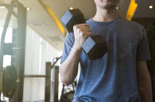 Obraz na plátně Young man beginner exercising with dumbbell flexing muscles at gym, sport traini