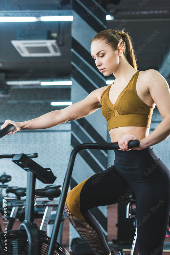 Fototapeta premium Young sportswoman doing workout on exercise bike in sports center