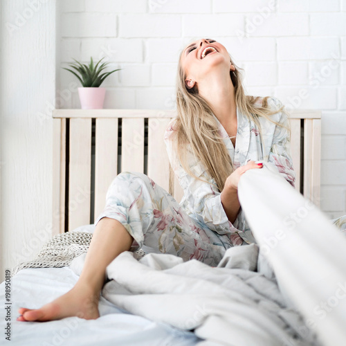 Laughing beautiful woman on the bed. She pulls the blanket on herself