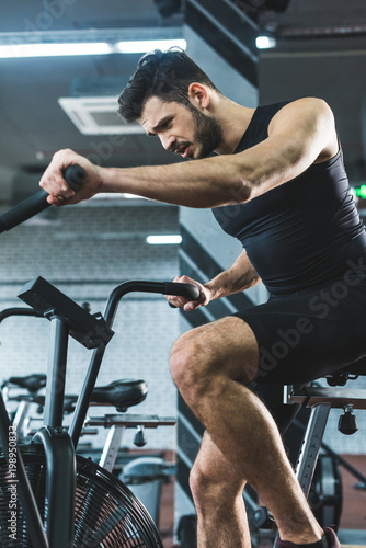 Young sportsman doing workout on exercise bike in sports center