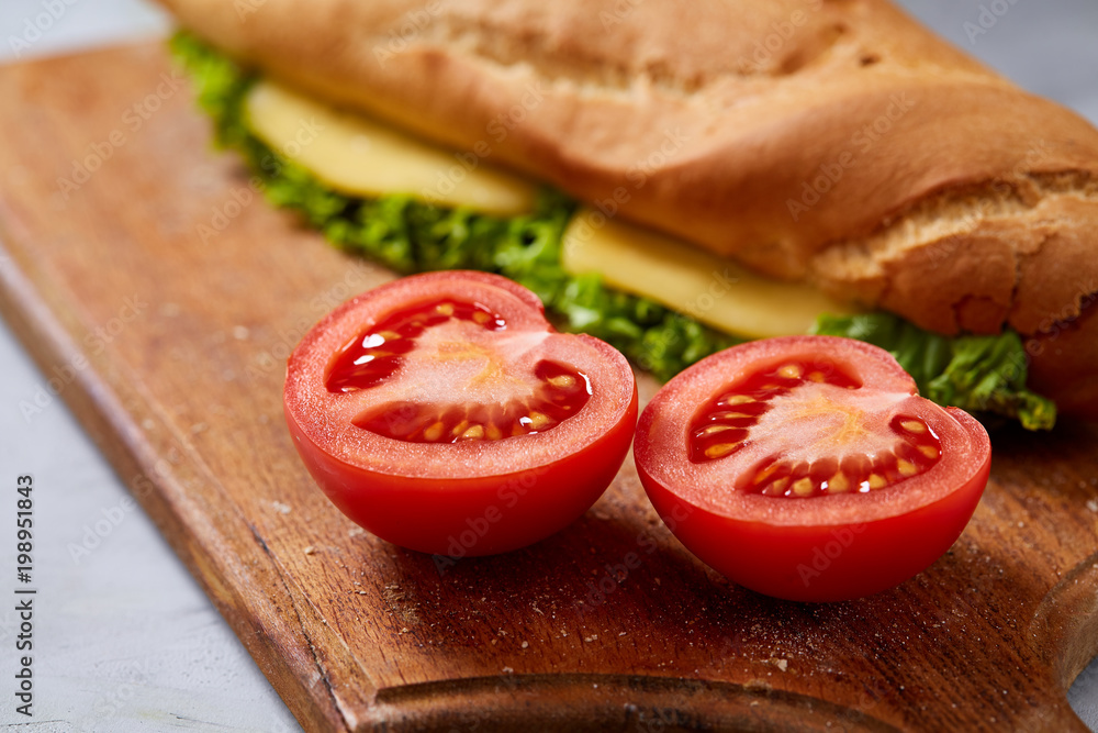 Fresh and tasty sandwich with cheese and vegetables on cutting board over white textured background, selective focus.