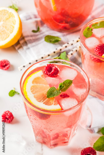 Summer refreshing drinks, fruit and berry raspberry mojito or lemonade with fresh mint, frozen raspberries, slices of lemon, ice, on a light background. copy space