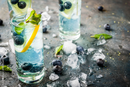 Summer refreshment drinks, Blueberry Lemonade or mojito cocktail with lemon, fresh blueberries and mint, sdark blue stone background copy space