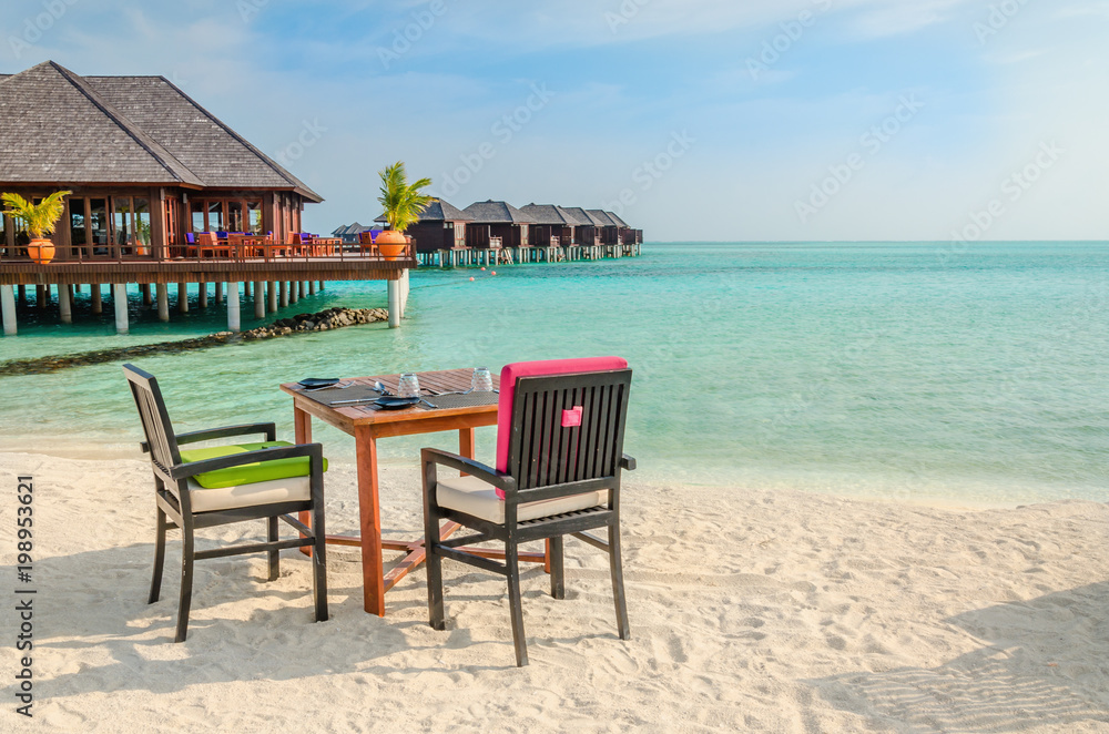 Table and chairs at restaurant at the background of water bungalows, Maldives island