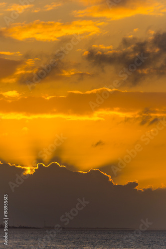 USA, Florida, Orange sunrays of sunset behind clouds at ocean water