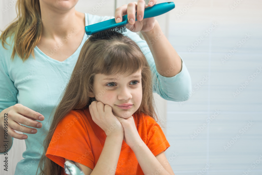 A beautiful daughter looks cute in the mirror while Mom combs her hair A beautiful daughter looks cute in the mirror while Mom combs her hair