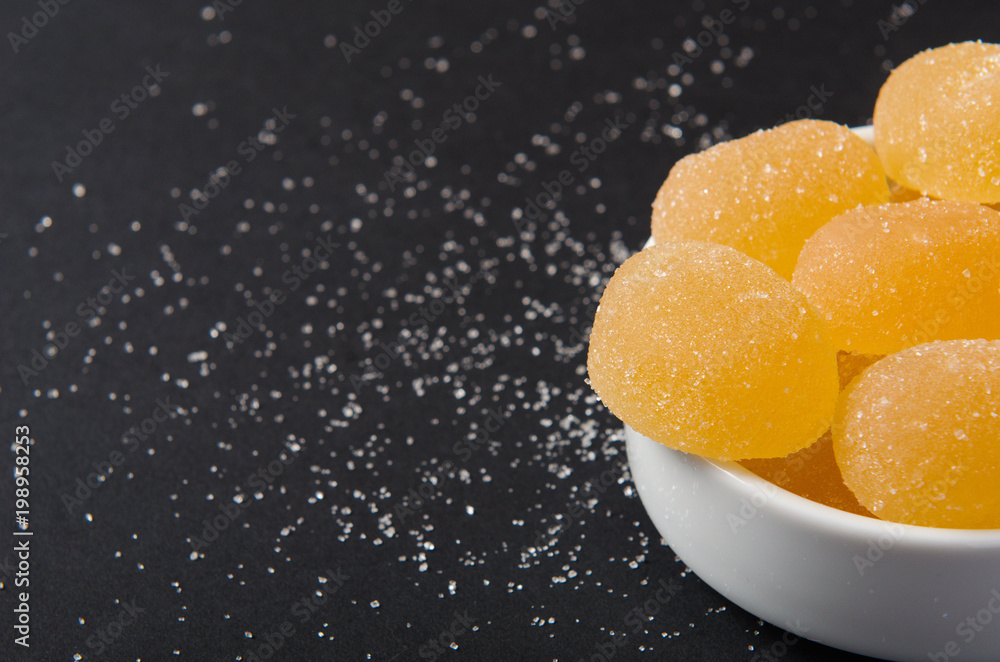 Marmalade. Yellow, orange candy, sprinkled with sugar in a white bowl on a black background. Copy space Marmalade. Yellow, orange candy, sprinkled with sugar in a white bowl on a black background. Copy space