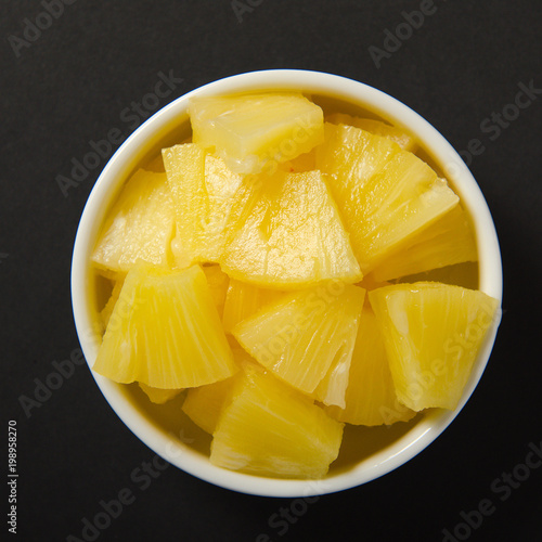 Wallpaper Mural Pieces of pineapple cut into slices in a white bowl. Ripe yellow sweet fruit on black background. Torontodigital.ca
