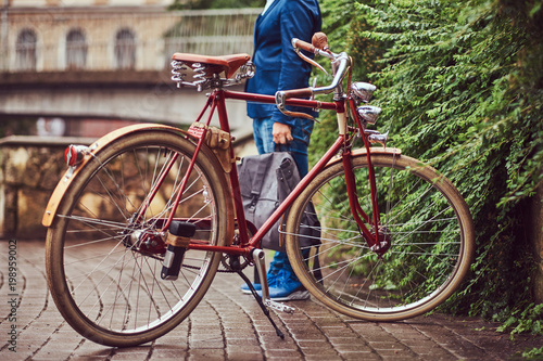 Male dressed in casual clothes, standing near a retro bicycle in a park.