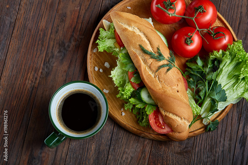 Fresh sandwich with lettuce, tomatoes, cheese on wooden plate, cup of coffee on wooden background, selective focus photo