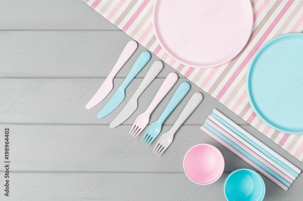 Set of empty, pastel plastic tableware bowls, spoons, knifes and forks isolated on gray wooden background. Flat lay, top view with minimal style. Set of empty, pastel plastic tableware bowls, spoons, knifes and forks isolated on gray wooden background. Flat lay, top view with minimal style.