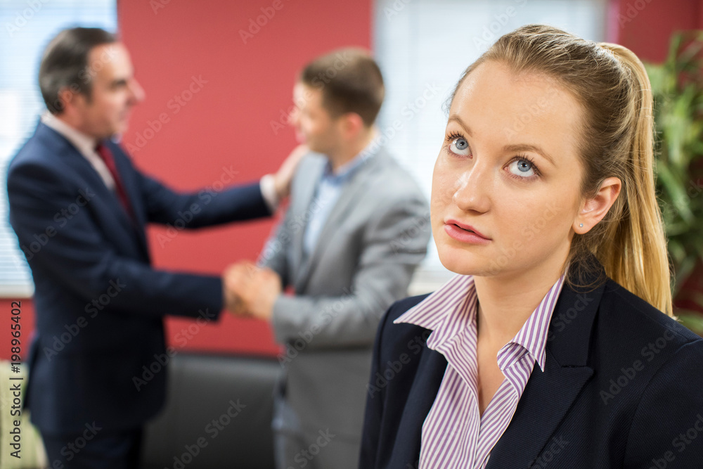 Unhappy Businesswoman With Male Colleague Being Congratulated Unhappy Businesswoman With Male Colleague Being Congratulated