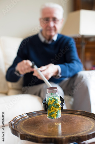 Senior Man Using Reaching Arm To Pick Up Medication At Home photo