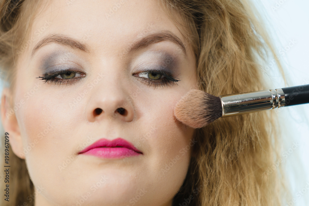 Makeup artist applying with brush rouge on female check Makeup artist applying with brush rouge on female check