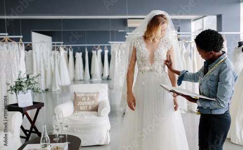 Dress designer fitting bridal gown to woman in boutique